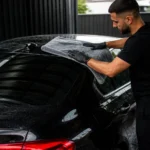 Secado de un coche negro a la sombra con una toalla de microfibra limpia